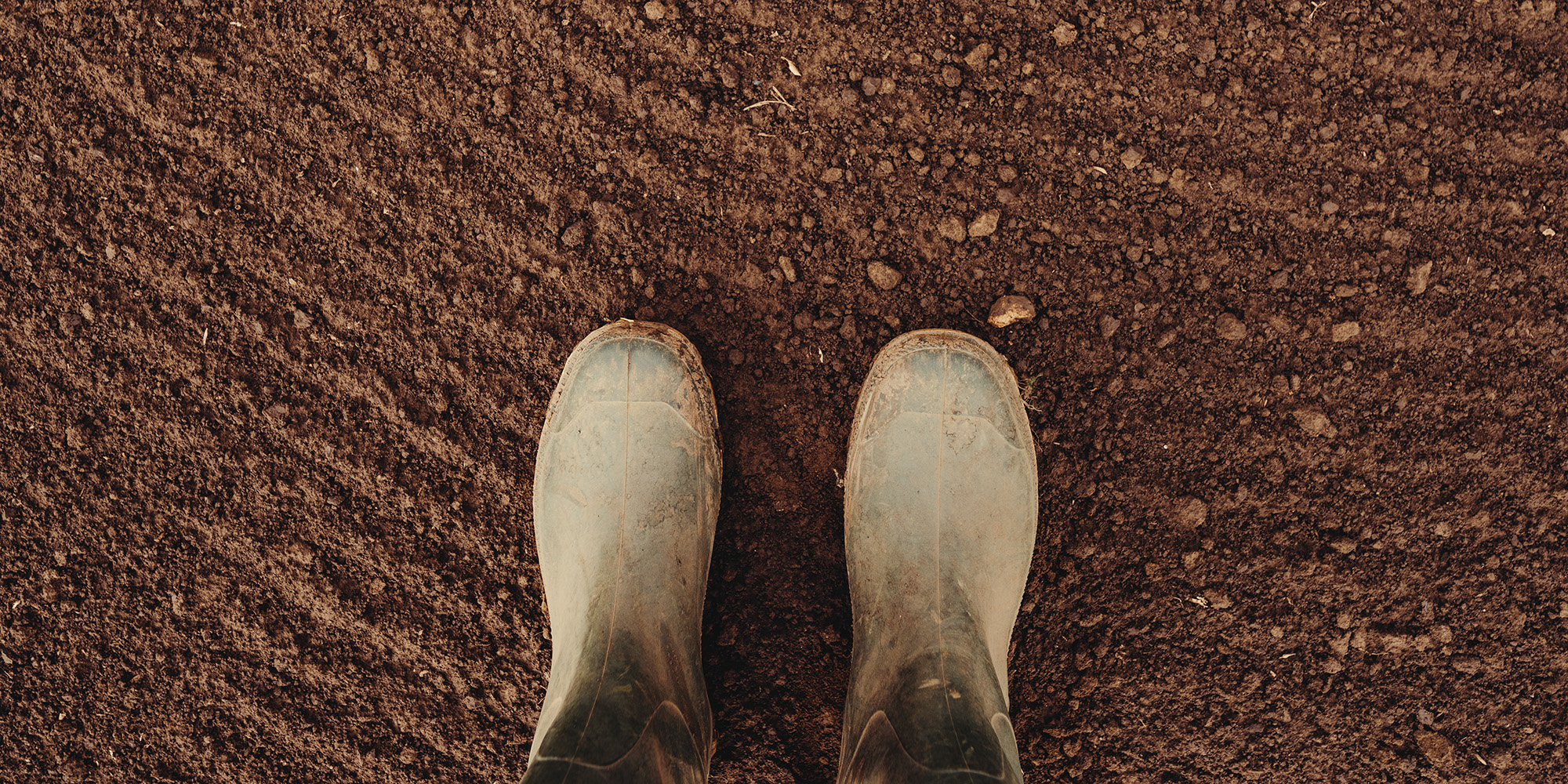 Brun jord sedd uppifrån och framdelen på ett par bruna stövlar.