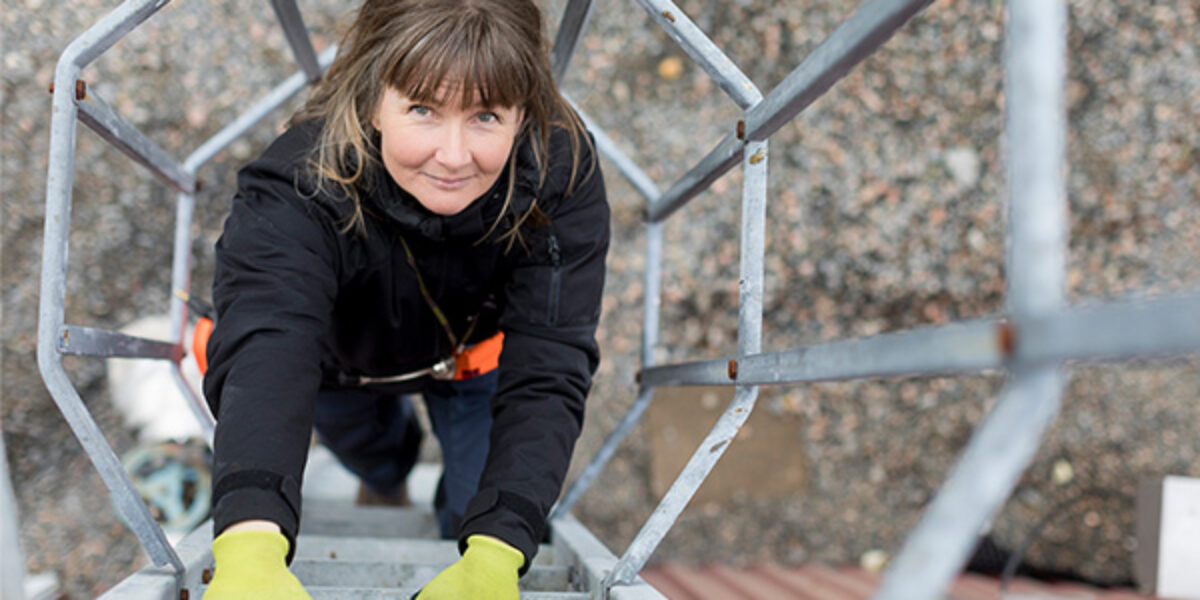 Sara Bergström Nilsson klättrar uppför en metallstege vid en biogasanläggning, med stålkonstruktion och grus i bakgrunden.