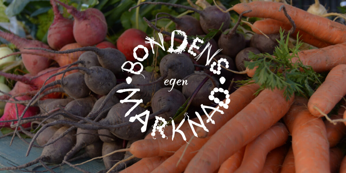 Morötter, rödbetor och gul lök ligger i högar på ett bord och visas som nyskördade grönsaker med blast. Ovanpå syns den vita, cirkelformade texten: “BONDENS egen MARKNAD”.