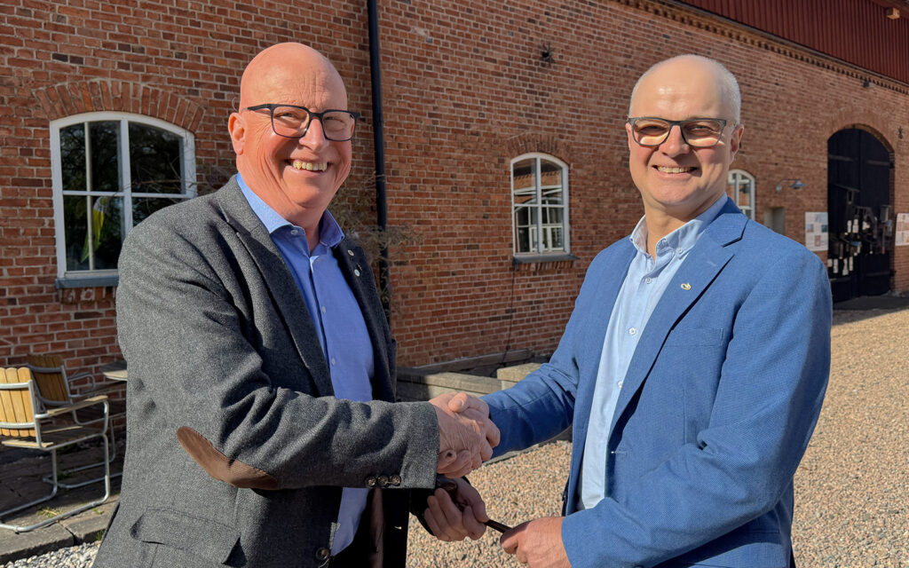 Svå män i kavaj skakar hand och den ena lämnar över en ordförandeklubba till den andra