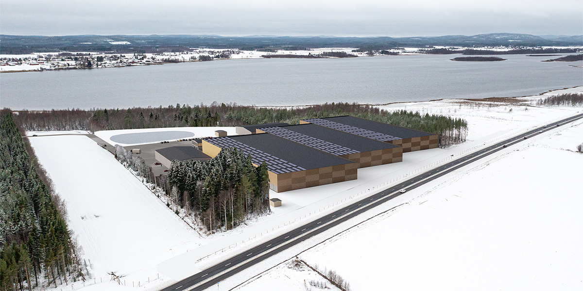 Drönarvy visar en inlagd illustration av en planerad fiskodlingsanläggning med flera stora hallar med solpaneler på taken, intill en väg och skog, omgiven av snötäckta fält vid en sjö.