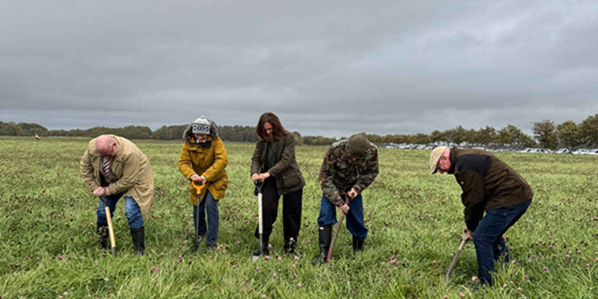 Fem personer tar det första spadtaget i en grön äng under en mulen himmel vid Lilla Böslid, i samband med starten för Hallands första solbruksanläggning.