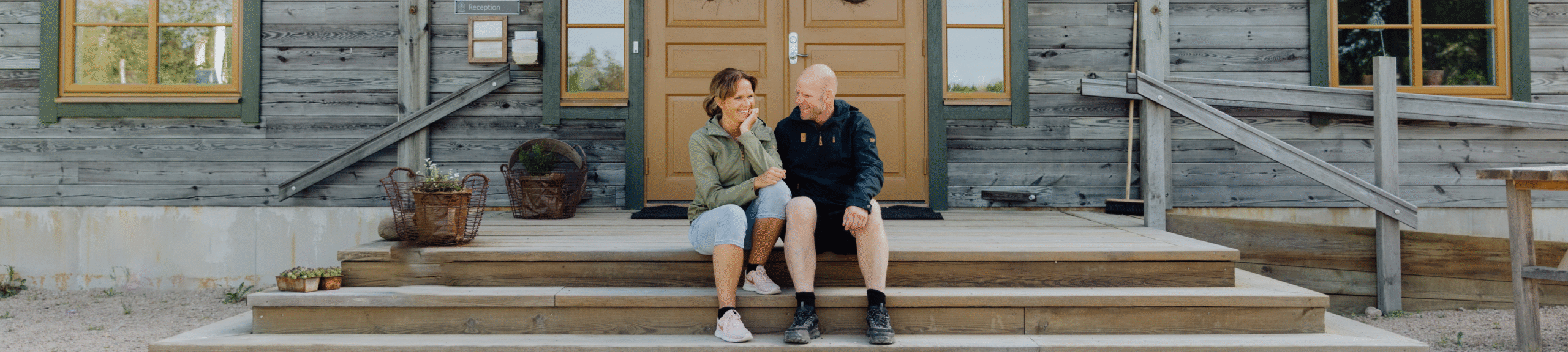 En kvinna och en man sitter framför ett trähus.