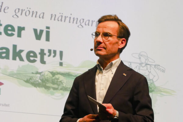 Statsministern ulf Kristersson står på scen. Skärm i bakgrunden med texten "nu flyter vi grässtaket"