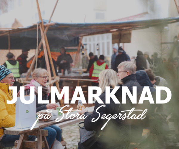 Besökare sitter och pratar vid träbord på en julmarknad utomhus, med marknadsstånd och folk i bakgrunden. Text på bilden: “JULMARKNAD på Stora Segeerstad”. Vinterklädda personer skapar en livlig, varm stämning.