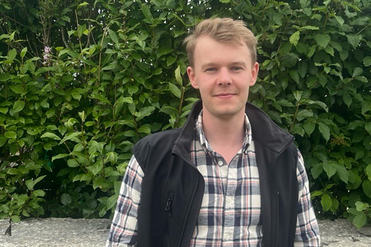 Ung man med rutig skjorta och svart väst. Ljust kort hår.