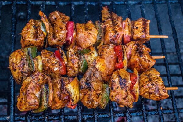 Grillspett med marinerade köttbitar och grönsaker grillas på ett svart grillgaller. Köttet har tydliga grillränder och är varvat med paprika och lök, medan glödens värme syns svagt under gallret.