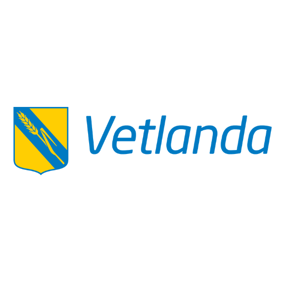 Blue “Vetlanda” wordmark sits beside a yellow-and-blue shield emblem with a diagonal blue stripe and a wheat stalk, presented on a black background as a municipal or organizational logo.