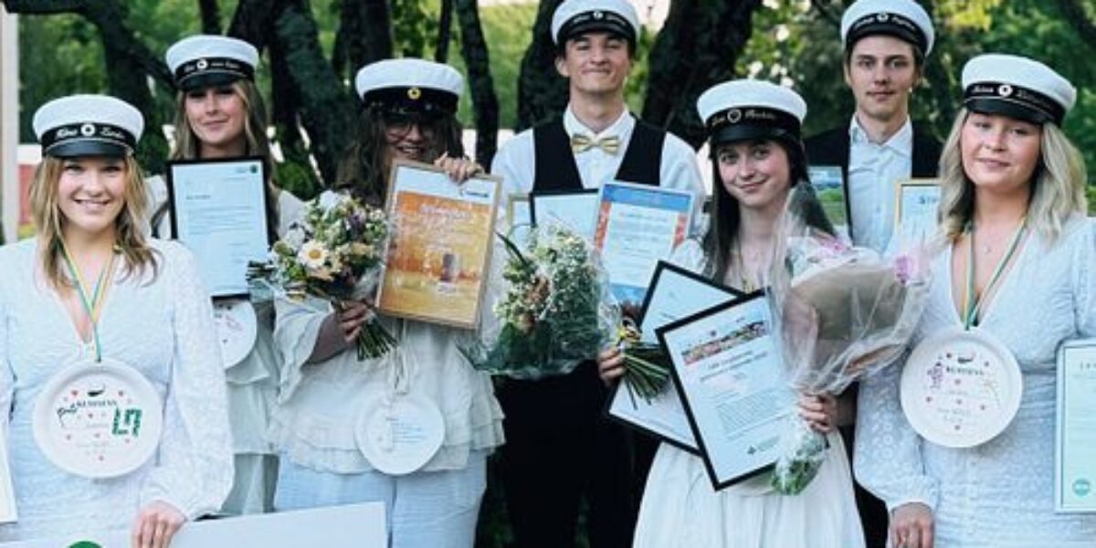 Group of graduates in white caps hold bouquets, diplomas, medals, and oversized checks outdoors under trees. Visible text includes “Handelsbanken dina” and handwritten names “Nordvik,” “Tretusenkronor 3.000,” “Selina Lillichök,” and “Dina försäkringar.”