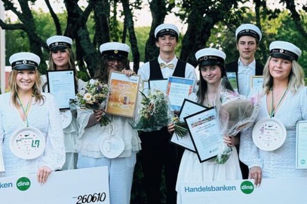 Group of graduates in white caps hold bouquets, diplomas, medals, and oversized checks outdoors under trees. Visible text includes “Handelsbanken dina” and handwritten names “Nordvik,” “Tretusenkronor 3.000,” “Selina Lillichök,” and “Dina försäkringar.”