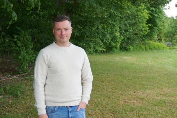 Man med vit tröja med skog och gräsmätta som bakgrund