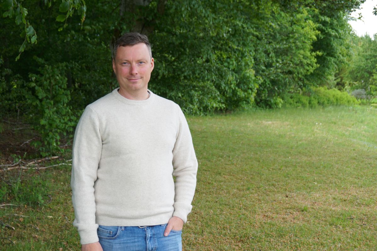Man med vit tröja med skog och gräsmätta som bakgrund