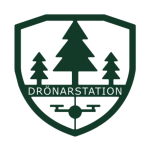 Mörkgrön sköldformad logotyp som visar tre stiliserade granar ovanför en enkel drönarsymbol; över motivet står texten “DRÖNARSTATION”. Designen är symmetrisk och ger ett natur- och tekniktema på mörk bakgrund.