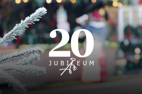 Snötäckt grankvist i förgrunden och suddig julmarknad med ljusslingor i bakgrunden; över bilden ligger texten “20 JUBILEUM År”, som markerar 20-årsjubileum i en vinterlig, festlig miljö.